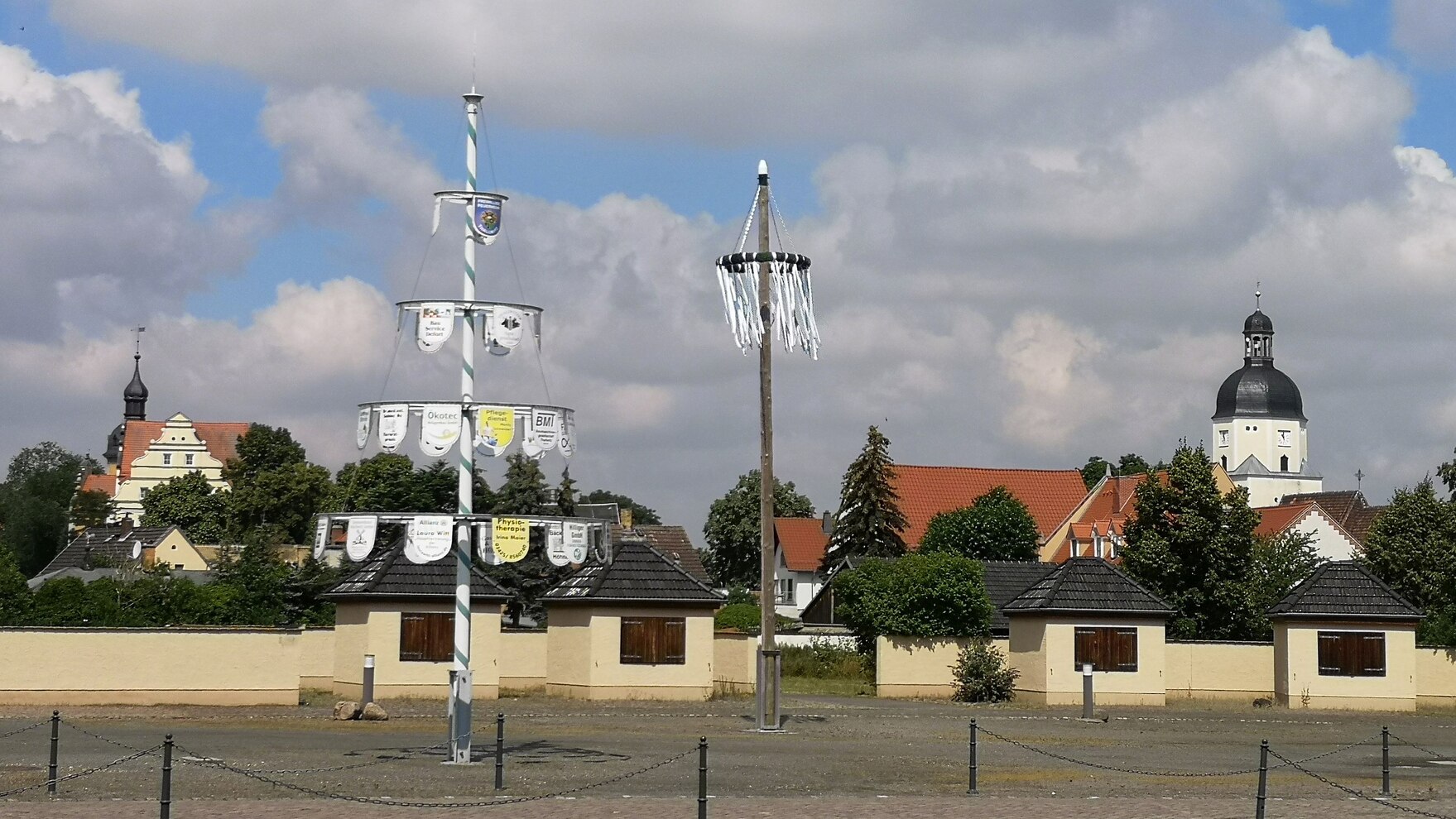 Maibaum und Kirche im Hintergrund, im Vordergrund ein Baum mit Gewerben der Gemeinde.