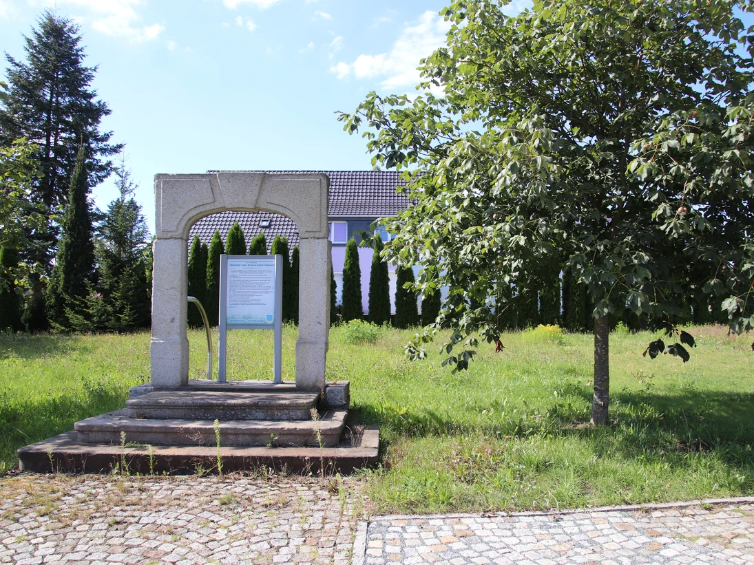 Treppenaufgang mit Granittürstock, dahinter schließt sich eine Wiese an, die von einer Hecke begrenzt wird