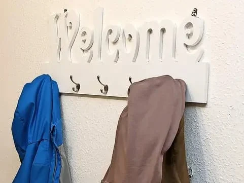 An einer Wandgarderobe mit dem Schriftzug Welcome hängen Jacken von Besuchern