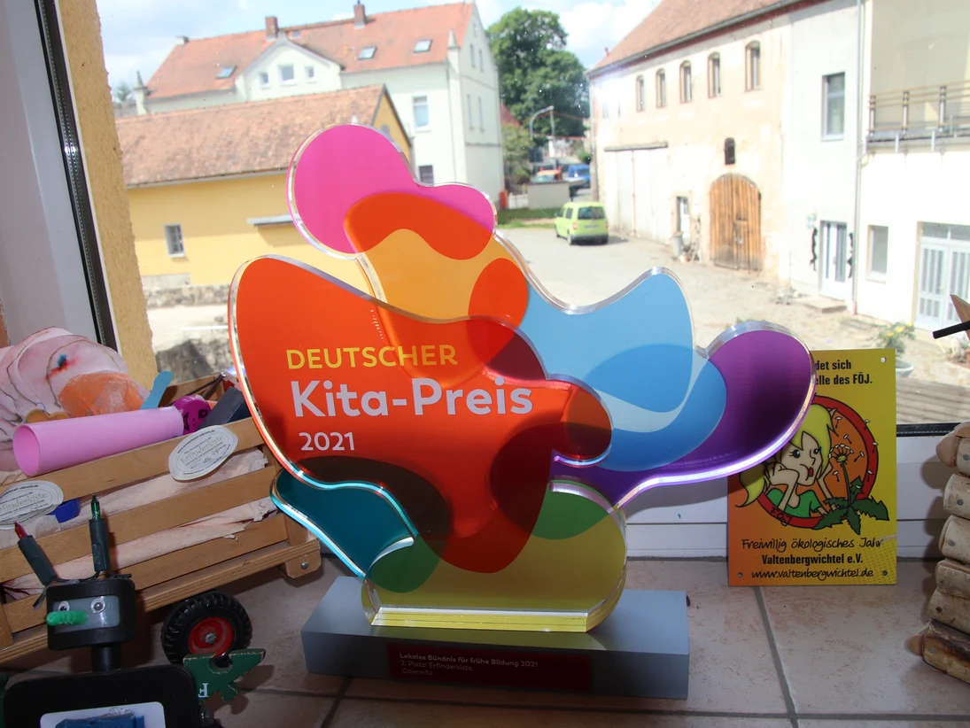 Deutscher Kita-Preis bestehend aus verschiedenfarbigen, durchscheinenden Plaste-Ellipsen und anderen Formen zwischen Gebasteltem aus Holz und anderen Materialien
