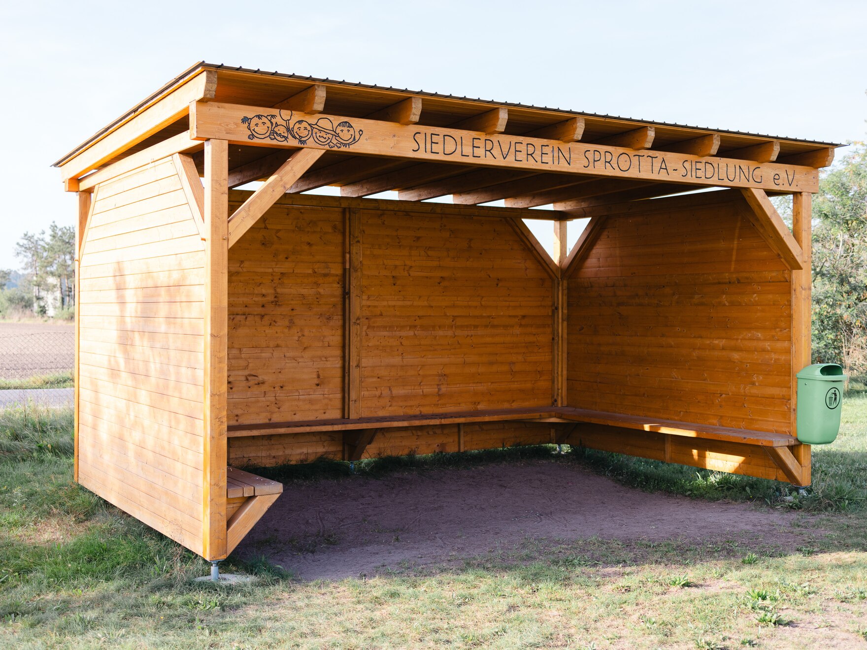 Die Schutzhütte aus Holz. Im Hintergrund Feld und Bäume.