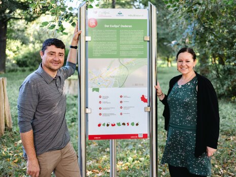 Zwei Personen präsentieren eine Informationstafel im "essbaren Wildpflanzenpark".