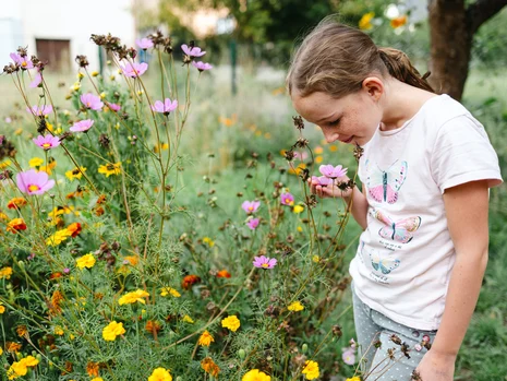 Ein Mädchen im Schulgarten beugt sich zu einer Blüte, um daran zu riechen.