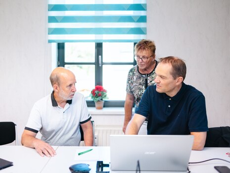 Drei Personen diskutieren vor einem Laptop im Schulungs- und Medienraum.