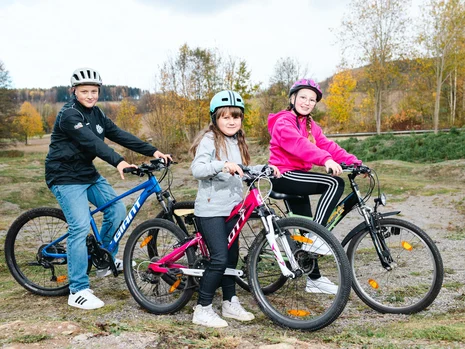 Drei Kinder stehen mit ihren Fahrrädern nebeneinander auf der neuen Pump-Track Strecke.