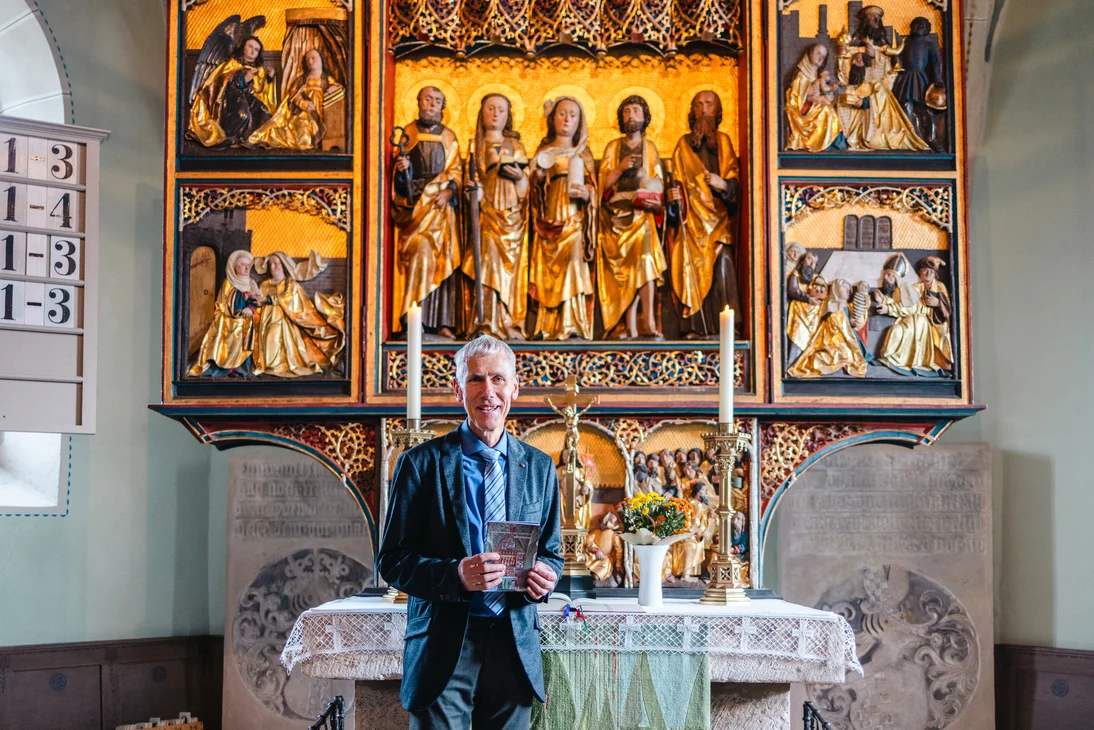 Der Pfarrer steht am Altar und hält das neue Altarretabel in der Hand.
