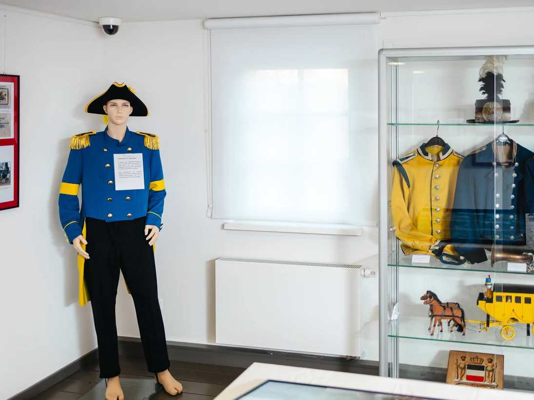 Blick in einen Raum, in dem ein Mannequin - welches die Uniform trägt- steht. Rechts davon ist eine Vitrine zu sehen, in der weitere Uniformen hängen.