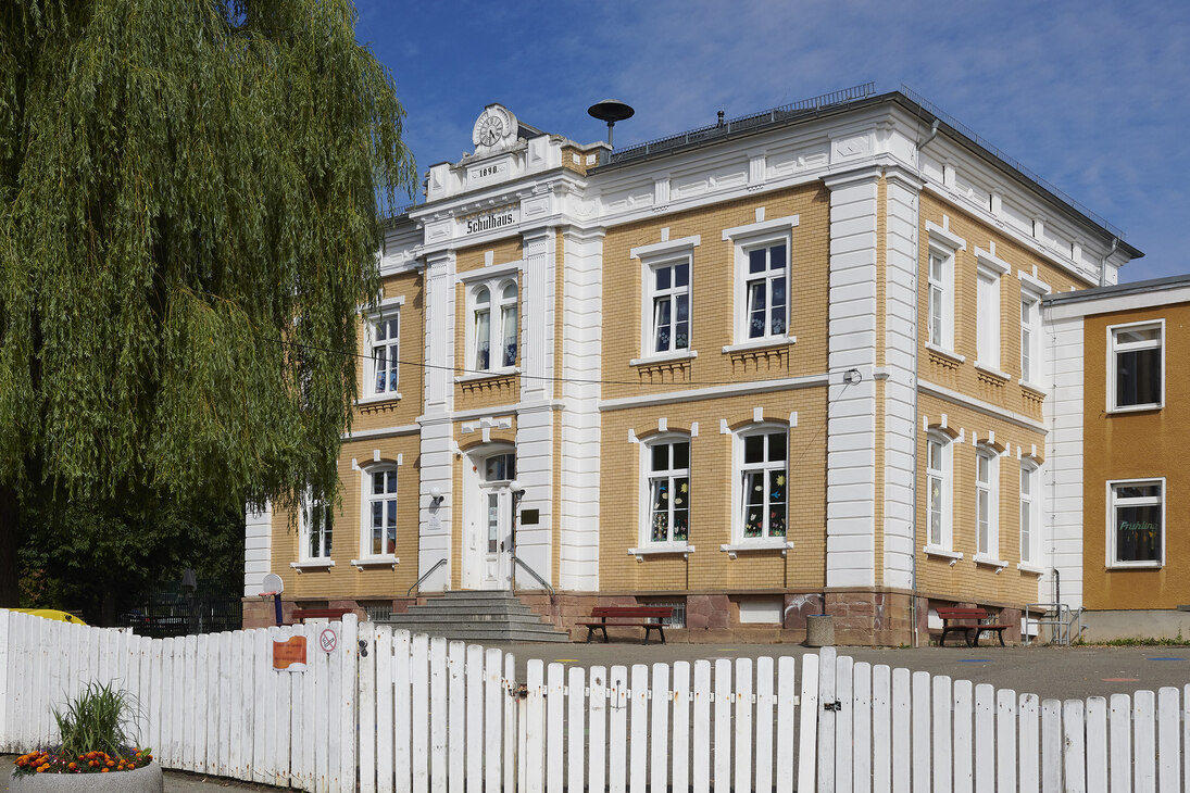 Das Schulgebäude, ein prächtiges Bauwerk aus der Kaiserzeit in gelb und weiß gehalten.