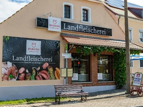 Straßenansicht der Landfleischerei mit großer Fensterfront und Werbefläche mit Produkten der Landfleischerei