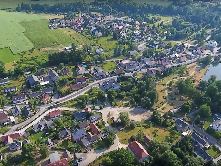 Luftaufnahme mit einer Hauptverkehrsstraße in der Mitte des Fotos, links und rechts der Straße Häuser, Felder und Grünzüge