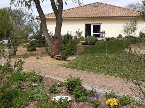 gepflegte Blumenbeete und ein im Weg vor einem flachen gelben Haus
