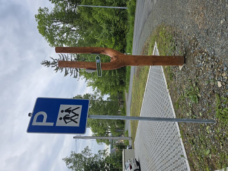 Wanderparkplatz mit blauem Parkplatzschild und hölzernem Wegweiser in Form einer Gabel mit grünem Schild 'Wernitzgrün' vor bewaldeter Umgebung.