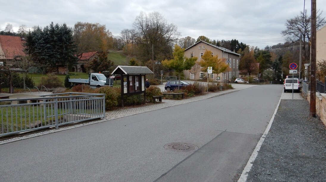 Park- und Rastplatz von der Straße aus gesehen, links der sanierte Bachlauf mit Geländer, Bushaltestelle