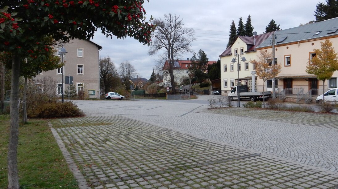 Platzgliederung mit unterschiedlichen Pflasterarten. Die Stellplätze für Fahrzeuge sind mit Rasenpflaster versehen.