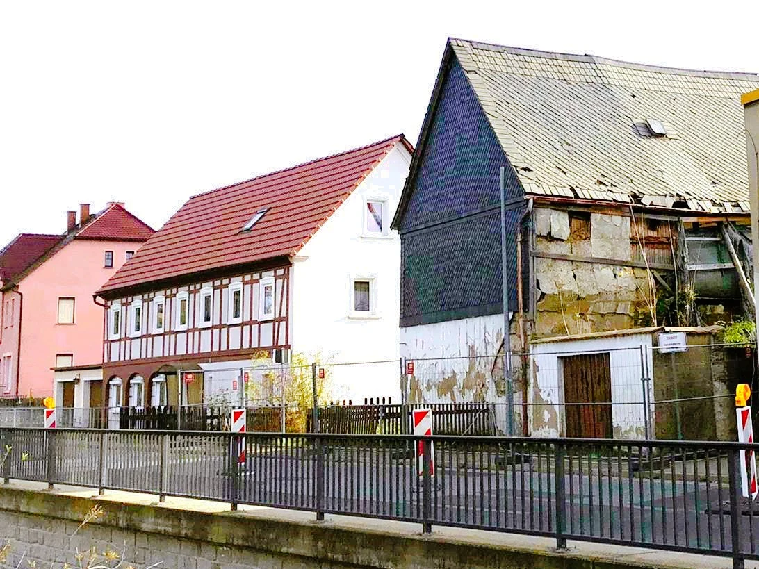 Teilansicht eines verfallenen Hauses, dem sich zwei sanierte Wohnhäuser anschließen