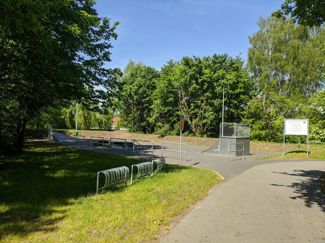 Blick auf Skateanlage mit Schanzen und Hindernissen in mitten von Bäumen, Fahrradständer davor