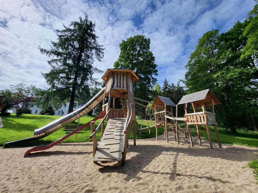 Neue Spielgeräte aus Holz mit Rutsche und Häuschen stehen auf sauberem hellem Sand