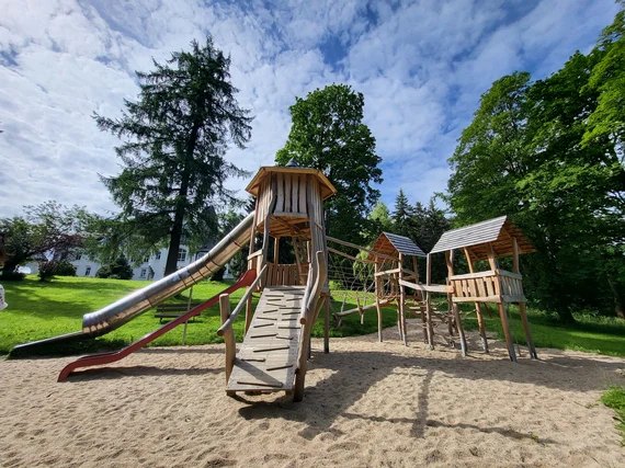 Neue Spielgeräte aus Holz mit Rutsche und Häuschen stehen auf sauberem hellem Sand