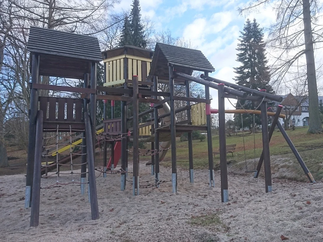 Alte Spielgeräte aus Holz stehen auf einem Spielplatz mit Sandboden