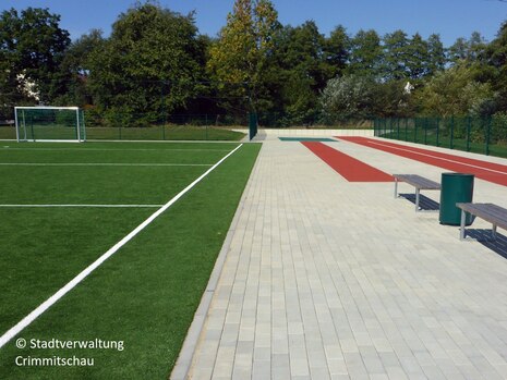 der neu modernisierte Sportplatz mit einer Kurzstreckenlaufbahn und einer Weitsprunganlage im Vordergrund, im Hintergrund die neue Kleinspielfläche mit Tor.