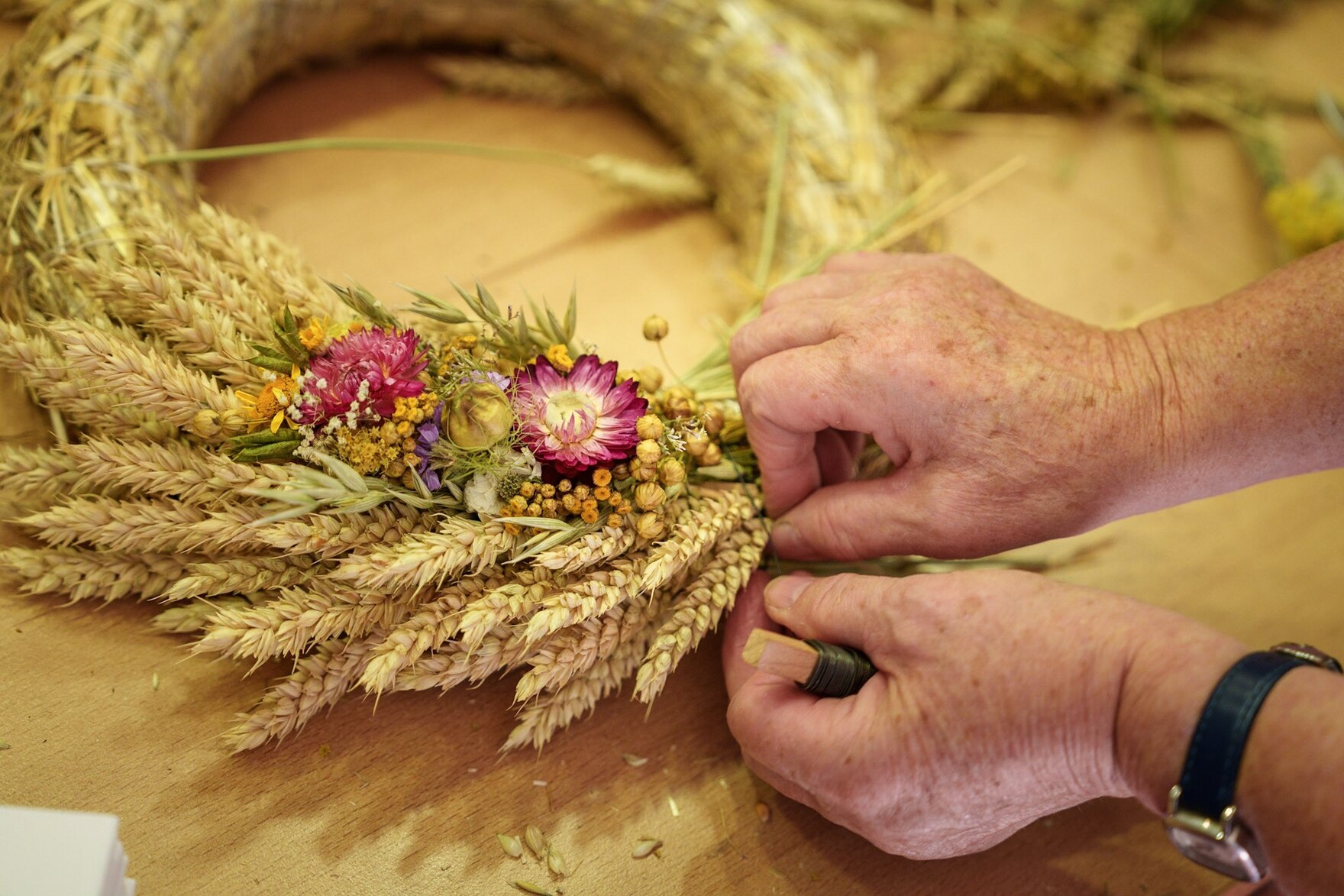 Hände befestigen Getreideähren und Trockenblumen an einem Erntekranz