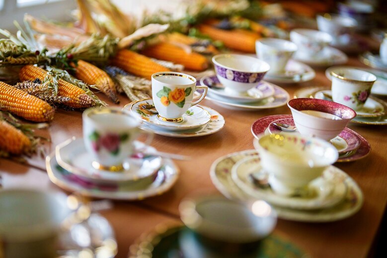 Bunte Sammeltassen auf einer Tafel mit Tischschmuck aus Maiskolben