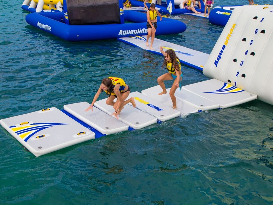 Zwei Mädchen balancieren über sechs schwimmende Einzelplattformen, die miteinander verbunden sind