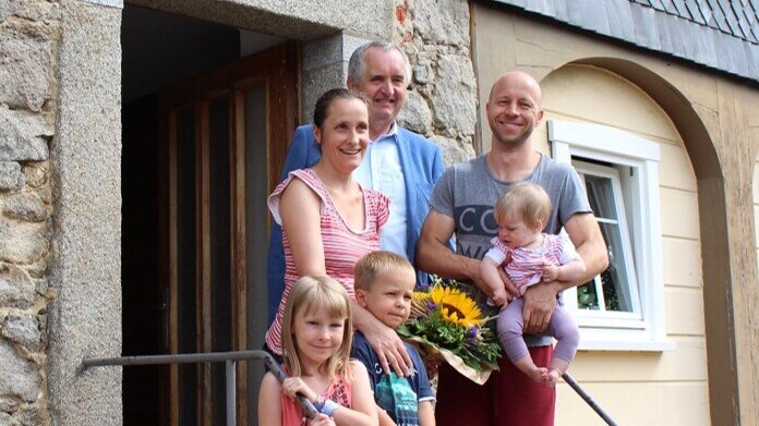 Junge Familie mit 3 Kindern und Herr Staatsminister Thomas Schmidt stehen vor einem denkmalgeschützten Umgebindehaus