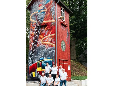 Mitglieder des Heimatvereins Leukersdorf stehen vor dem alten Schlauchturm Leukersdorf, welcher bunt bemalt ist.